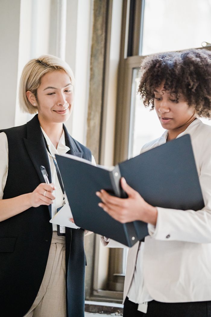 Contact Two diverse businesswomen collaborating on documents in modern office setting.