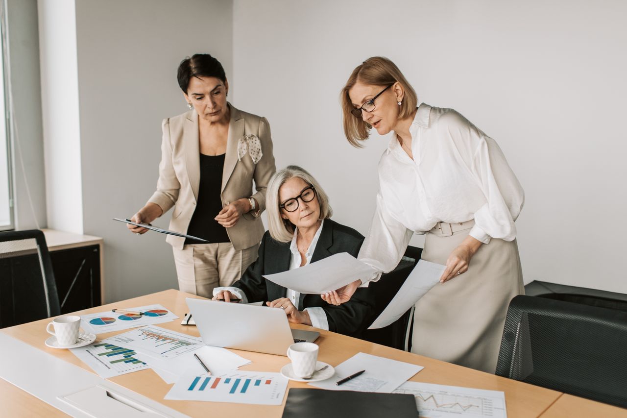 Services Three businesswomen discussing reports in a modern office environment.