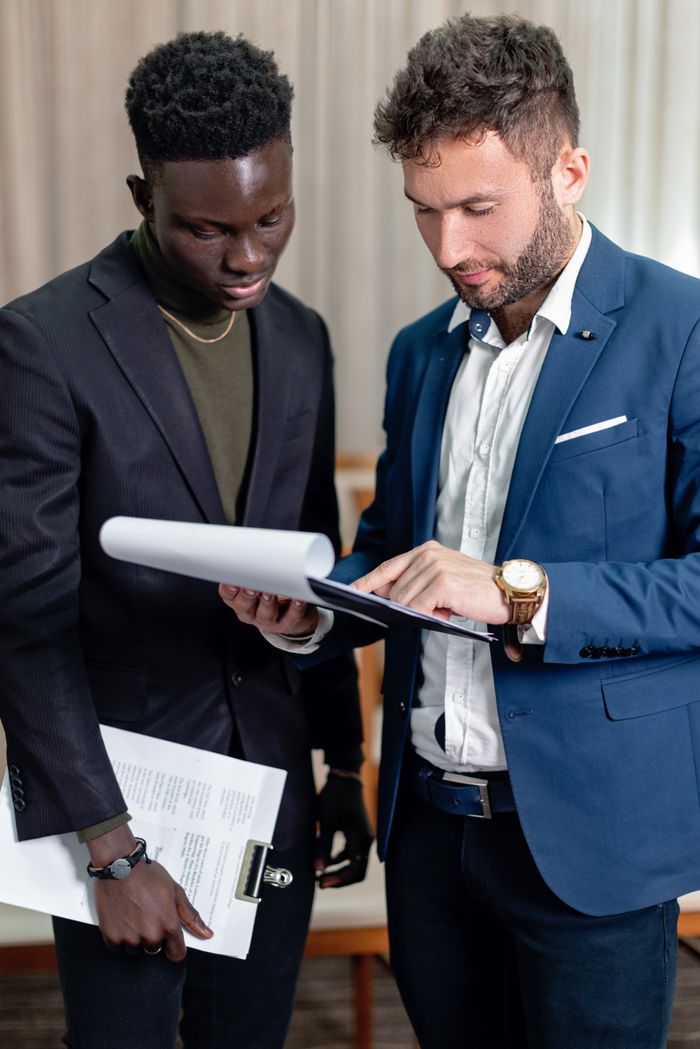 About Two business professionals in corporate attire reviewing documents indoors.